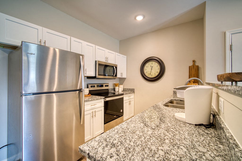 2 Bedroom Apartments in Boiling Springs, SC - Peachtree Village - Kitchen with Wood-Style Flooring, White Cabinetry, Stainless Steel Appliances, Clock, and Recessed Lighting.
