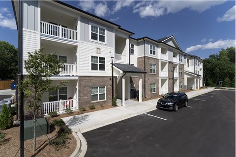 A black car is parked in a parking lot in front of a white apartment building.