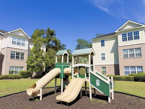 A playground with a green slide and a white railing in front of apartment buildings.