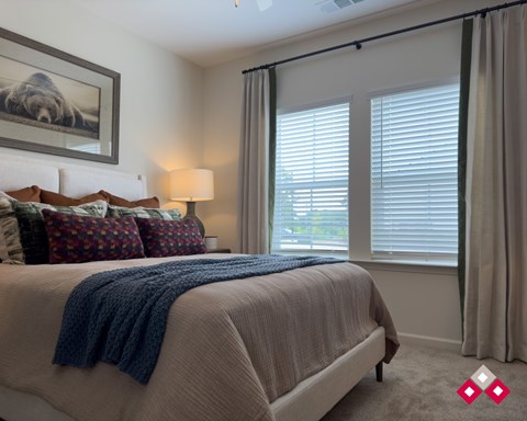 A bedroom with a large bed and a window with blinds.