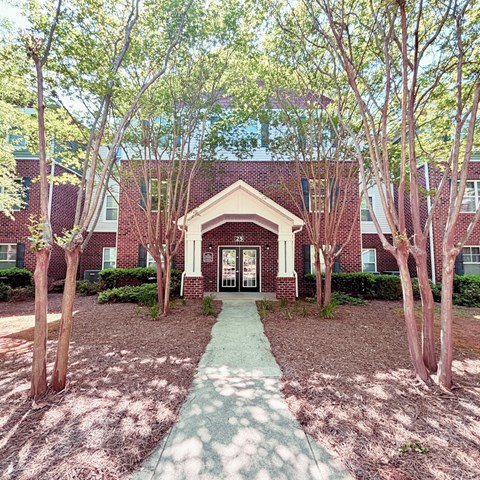 A red brick building with a white door and a green pathway leading to it.