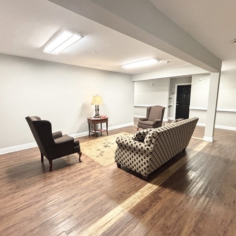 A living room with a black chair, a patterned sofa, and a small table with a lamp.