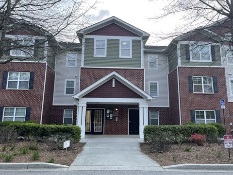 A brick building with a red door and a sign in front.