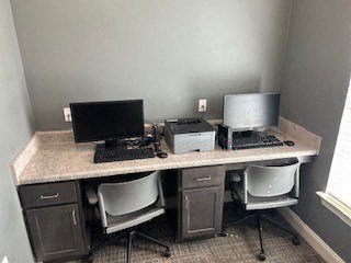 A workspace with a desk, two chairs, a laptop, a monitor, a keyboard, and a mouse.