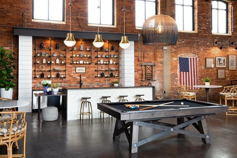 A pool table is in the middle of a room with a brick wall and a bar area.