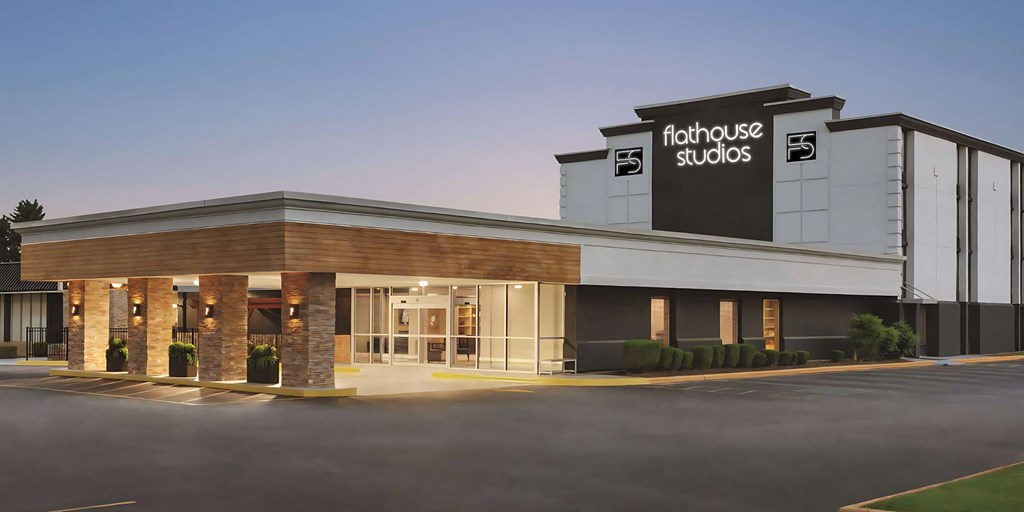 1-bedroom Apartments in Greenville, SC - Flathouse Studios - Exterior Street View of Flathouse Studios with Stone Details, White Walls, Large Logo, and Landscaped Bushes