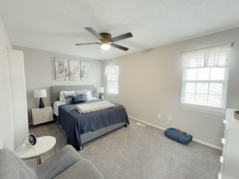Reserve at Hillcrest model unit staged bedroom with blue blankets, gray chair, two windows with curtains and a dog bed