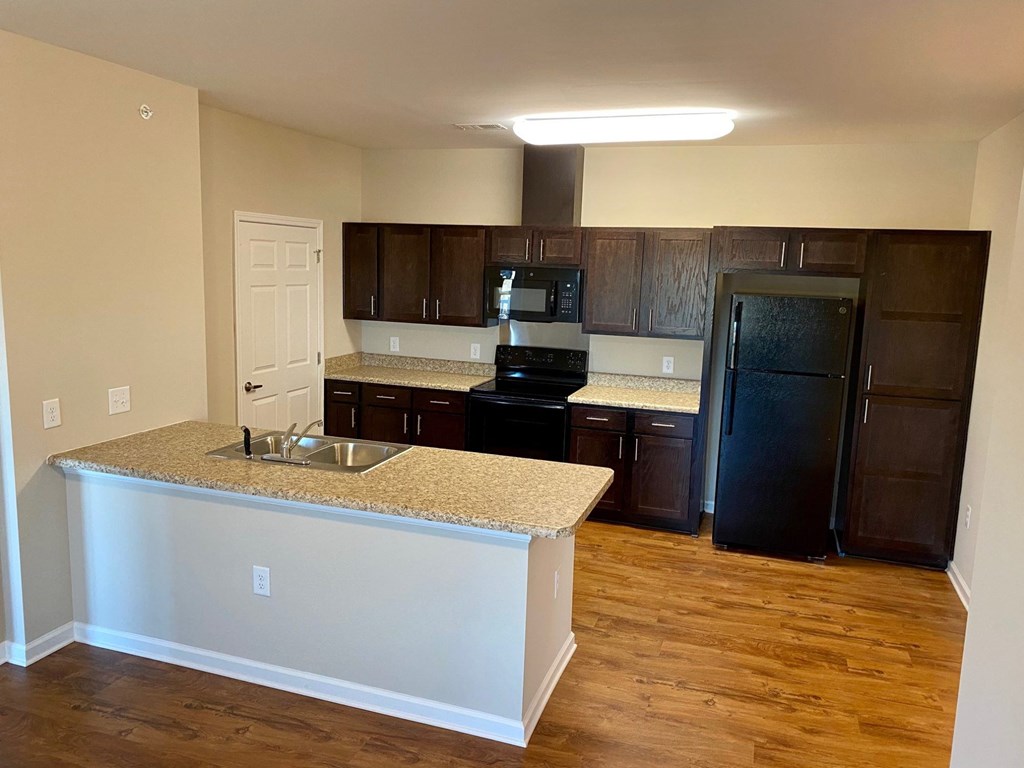 The kitchen of Linden Square apartments, with a granite countertop a black refrigerator, an oven, a microwave and a sink with a disposal.