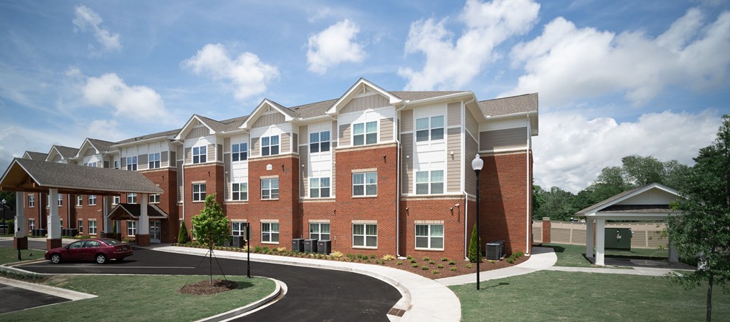 A large brick apartment building with a red car parked in front.