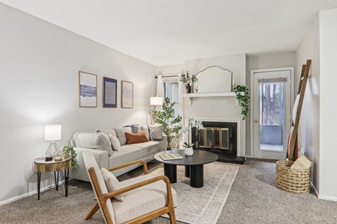 Plantations at Haywood staged living room with carpet, couch, ladder blanket, chairs and attached kitchen.
