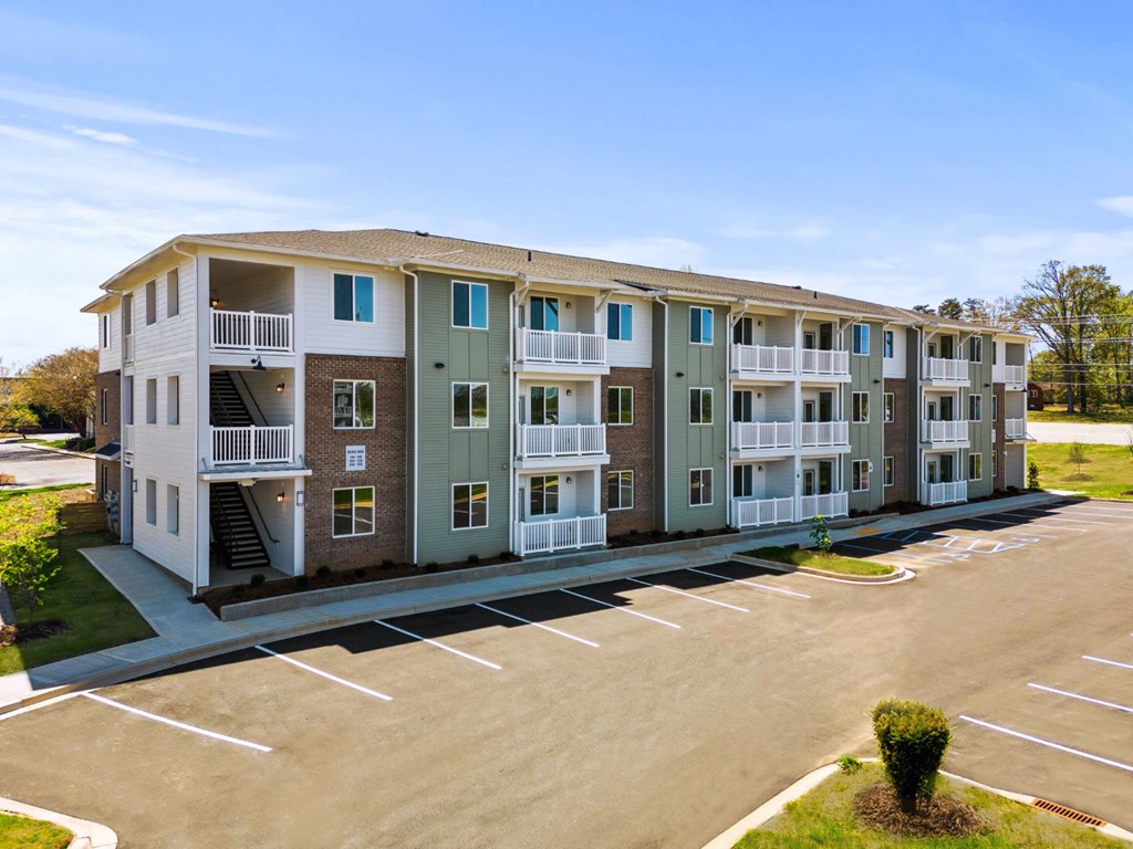 One Bedroom Apartments in Greenville SC - Alston - Exterior of One of the Property Buildings with Three Levels and Private Balconies, with a Parking Lot in Front