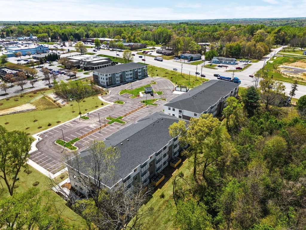 A large building with a grey roof is surrounded by trees and other buildings.