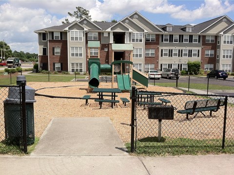 A playground area with a green slide and picnic tables surrounded by a black fence.