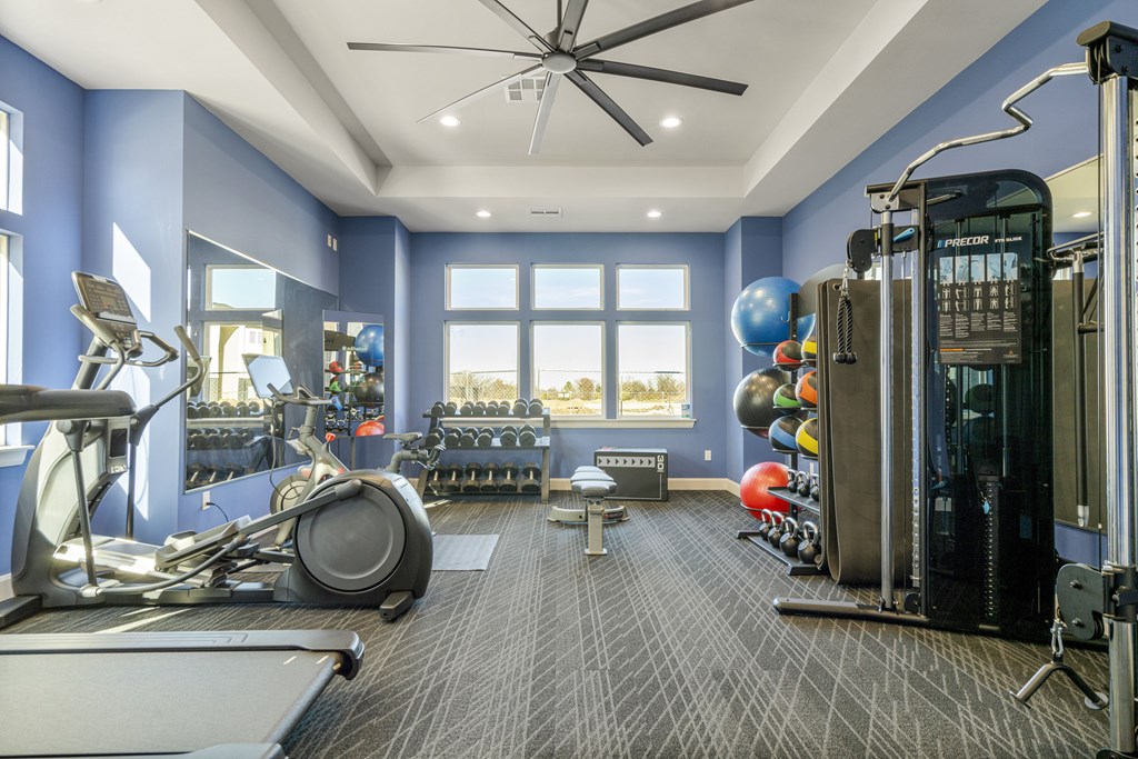 A spacious gym with a variety of equipment and a fan on the ceiling.