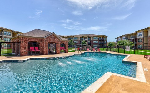 A large swimming pool in front of a brick building with a black fence around it.