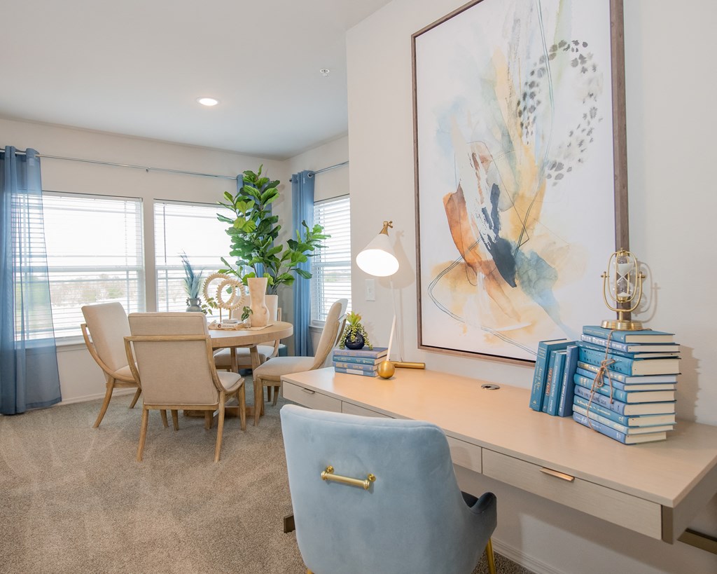 A room with a desk, chairs, and a painting on the wall.