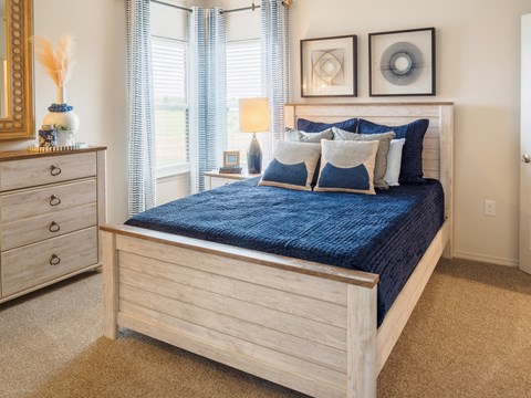 A bed with a blue comforter and matching pillows sits in a room with a wooden dresser and a mirror.