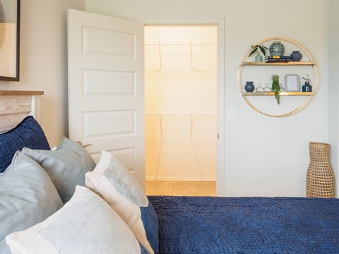 A bedroom with a bed, pillows, and a shelf with plants and decorative items.