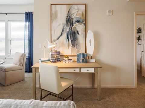 A room with a desk, chair, and a painting on the wall.