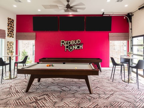 A pool table in a room with a red wall and a ceiling fan.