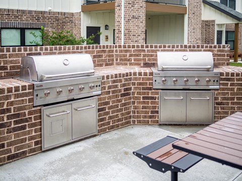 Two grills are on a brick patio.