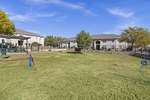 A grassy field with a red rope in the foreground and houses in the background.