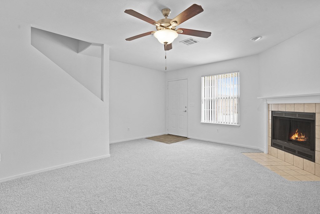 A room with a fireplace, a ceiling fan, and a window with blinds.