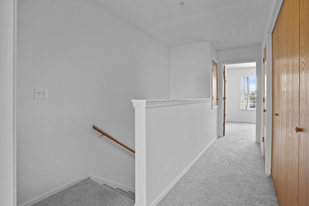 A long hallway with a carpeted floor and a wooden staircase.