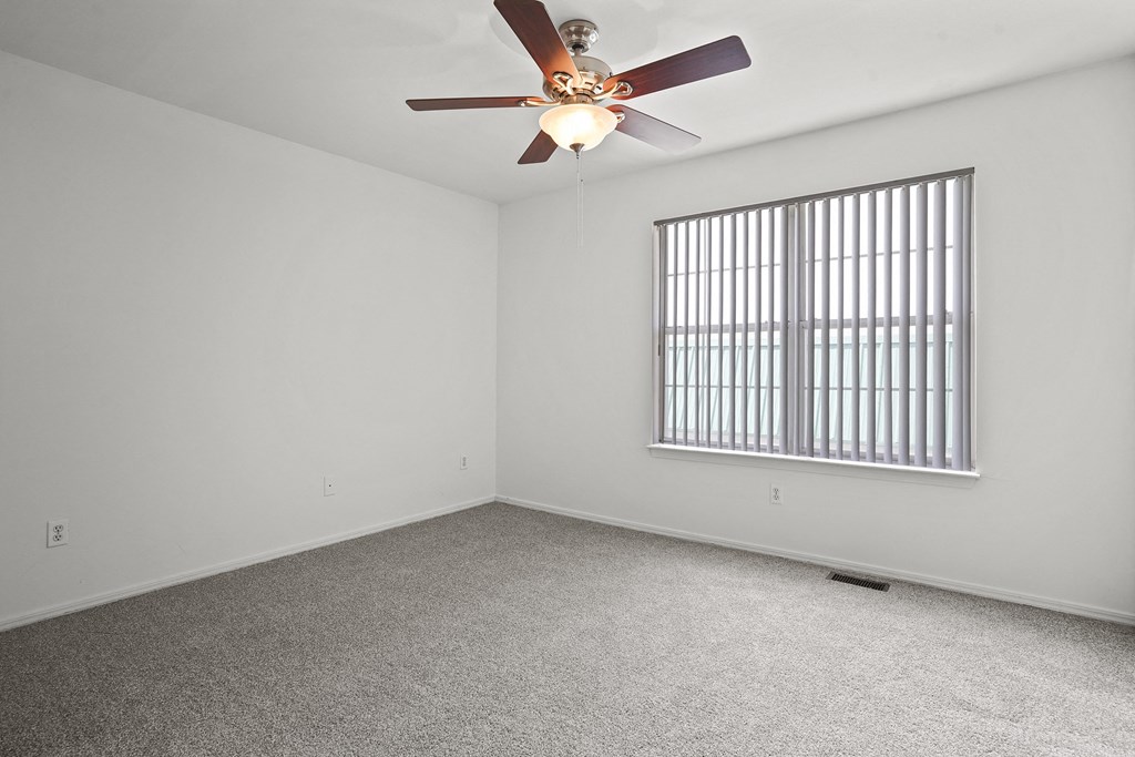 A room with a ceiling fan and a window with bars.