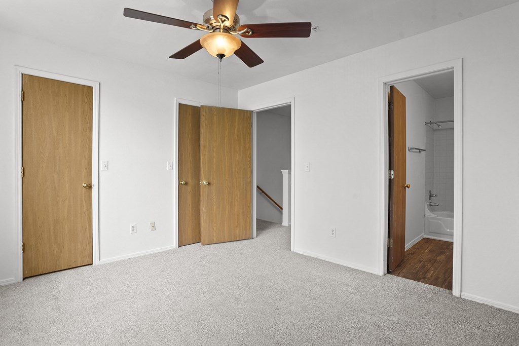 A room with a ceiling fan and three doors.