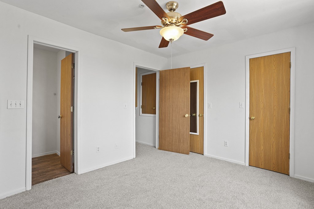 A room with a ceiling fan and four doors.
