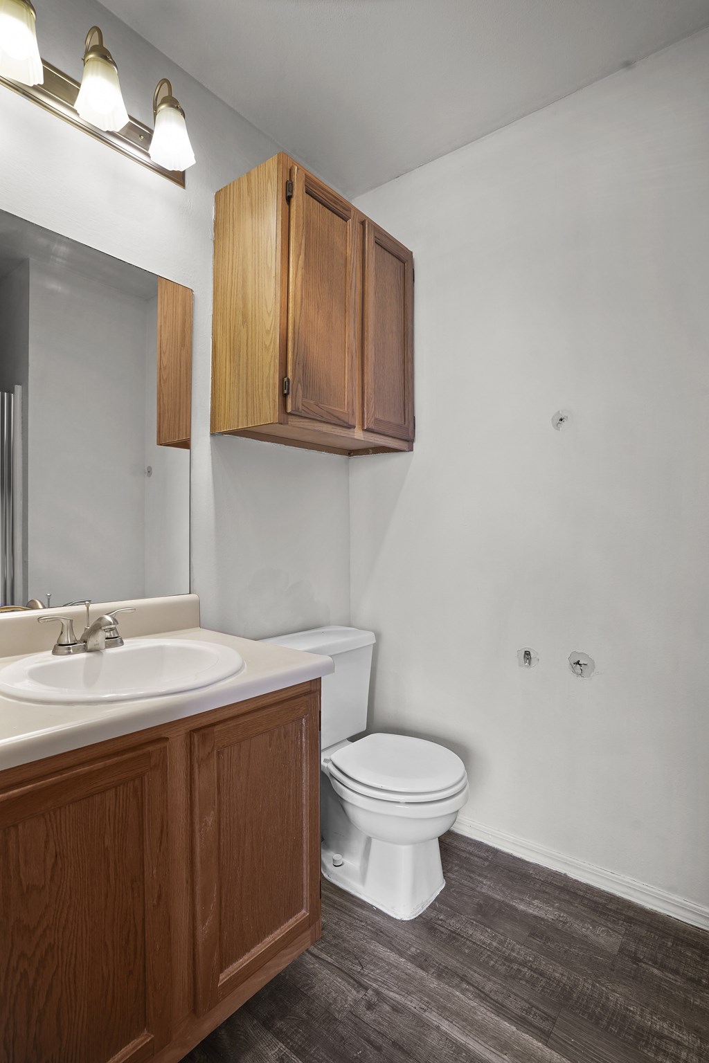 A white toilet sits in a bathroom with a wooden cabinet and a sink.