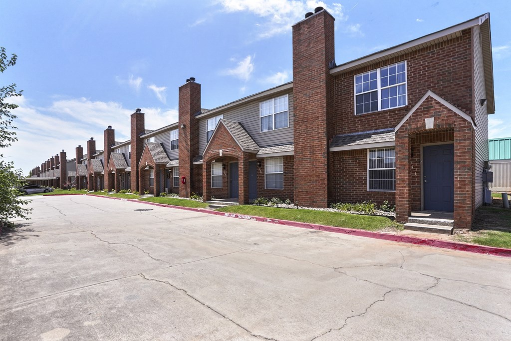 A row of red brick houses with a cracked grey parking lot in front.