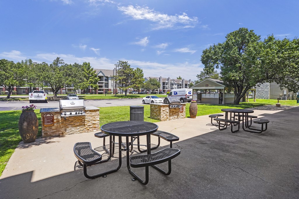 A black picnic table with four chairs is in the foreground of a sunny park.