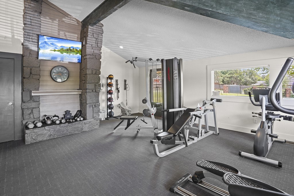 A well equipped home gym with a television and a fireplace.