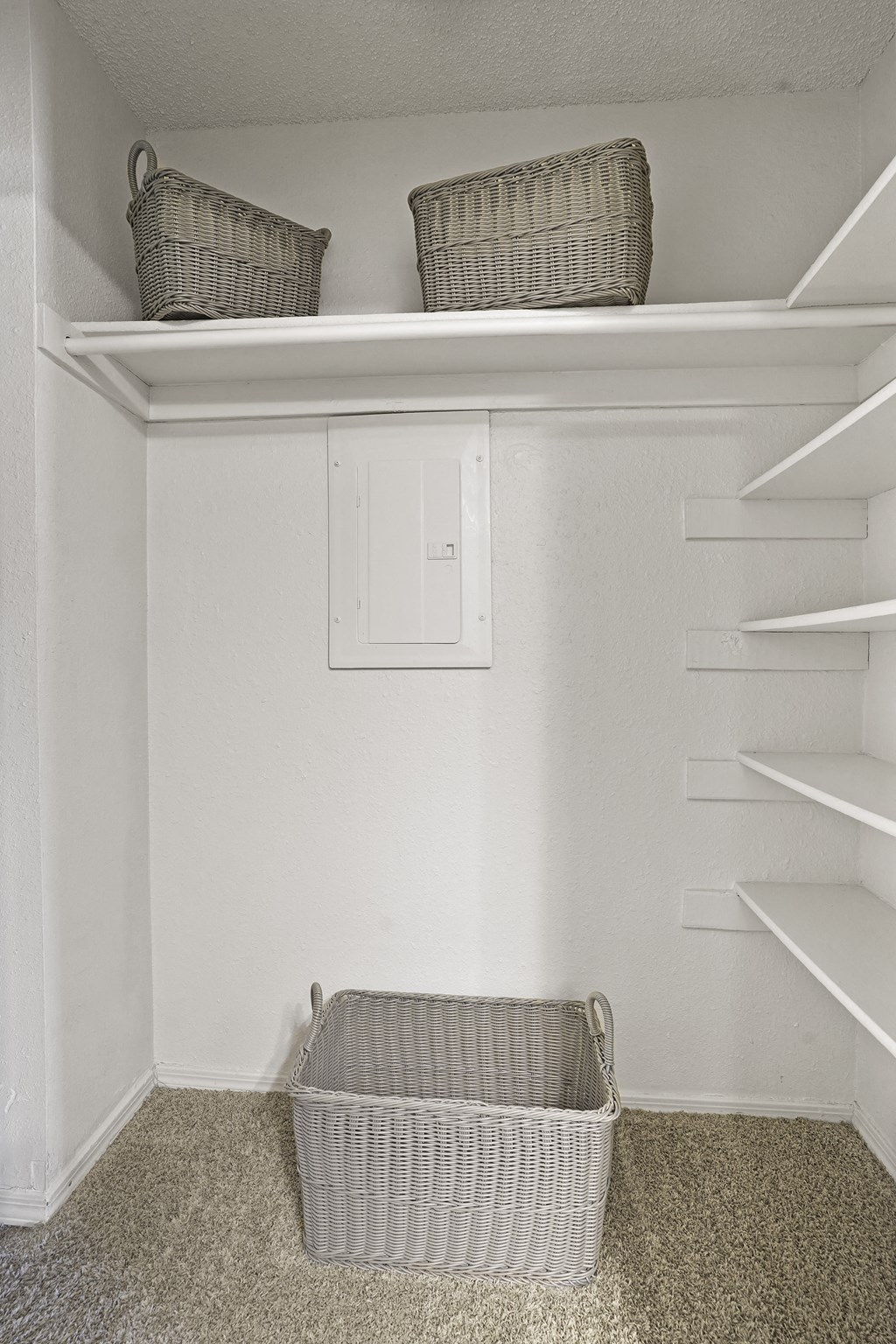 A white closet with a basket on the floor.