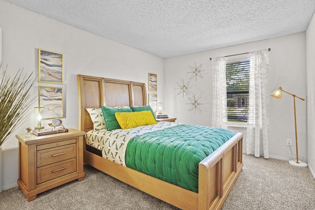 A bedroom with a bed, nightstand, and a window with white curtains.