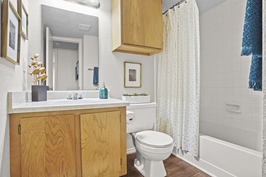 A white toilet sits in a bathroom with a wooden cabinet and a white sink.