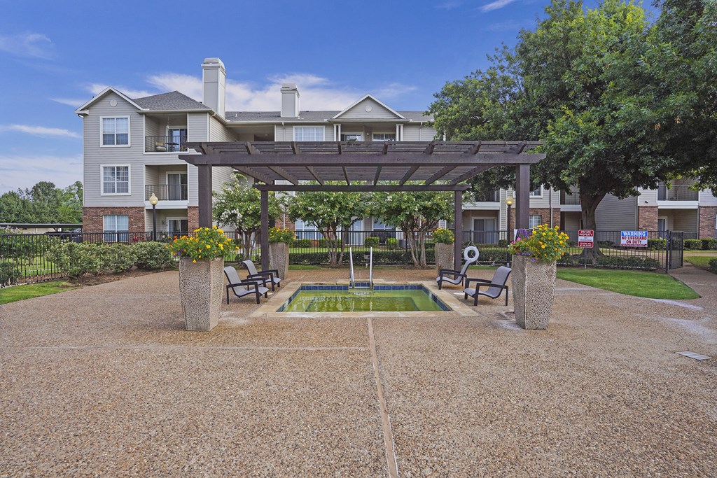 A patio area with a table and chairs is surrounded by a gravel area and a grassy area with a building in the background.