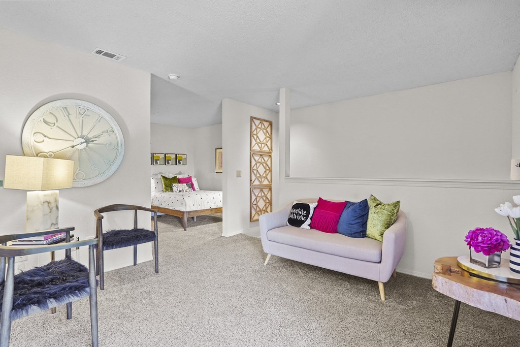 A living room with a white couch, a grey chair, a table with a vase of flowers, and a large clock on the wall.