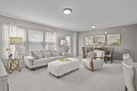 A living room with a white couch, a white ottoman, and a white chair.
