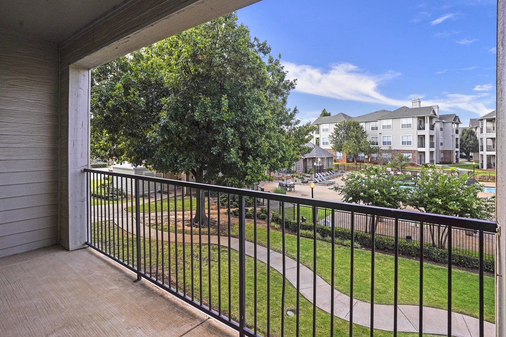 A balcony with a black railing overlooks a grassy area and apartment buildings.