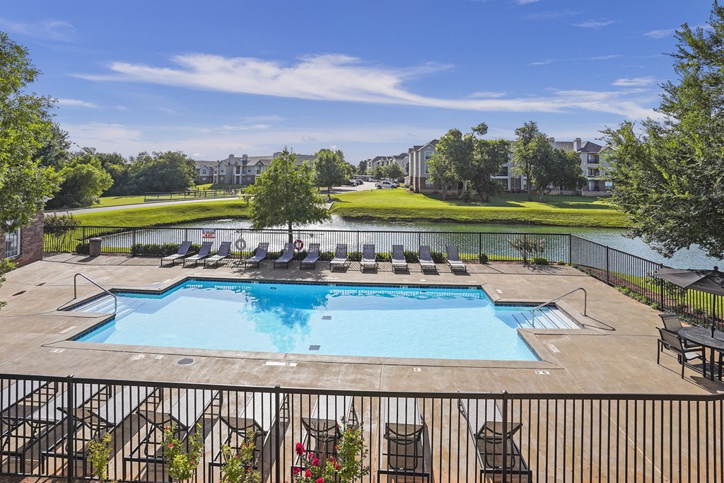 A large outdoor swimming pool surrounded by a black fence and lounge chairs.