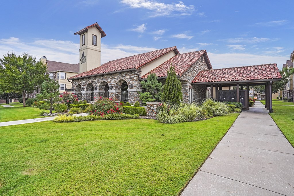 A building with a clock tower is surrounded by a well-kept lawn and a walkway.