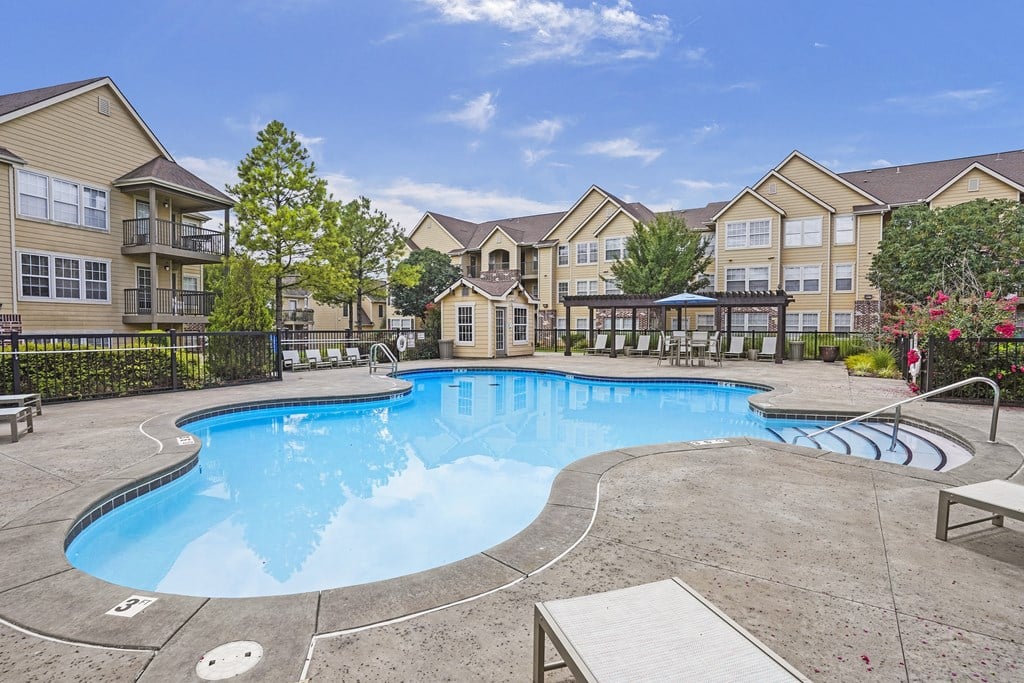 A large swimming pool surrounded by a concrete patio and a black fence.