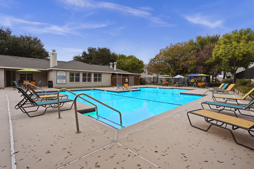 A pool surrounded by chairs and trees.