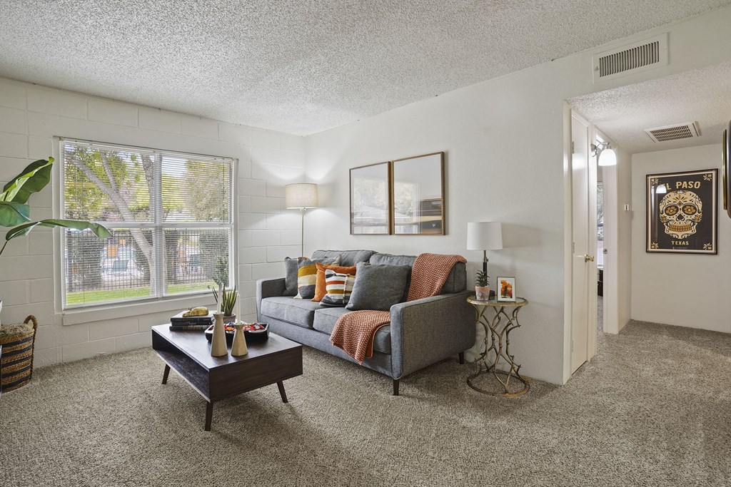 A living room with a grey couch, a coffee table, and a large window.