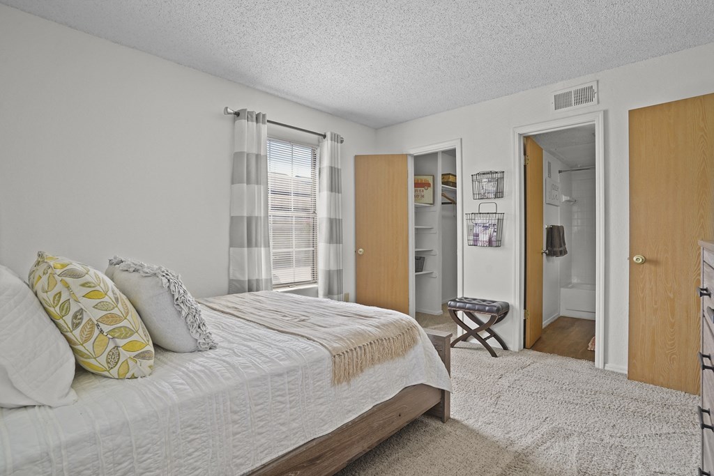 A bedroom with a bed, a window with curtains, and a small table with a chair.
