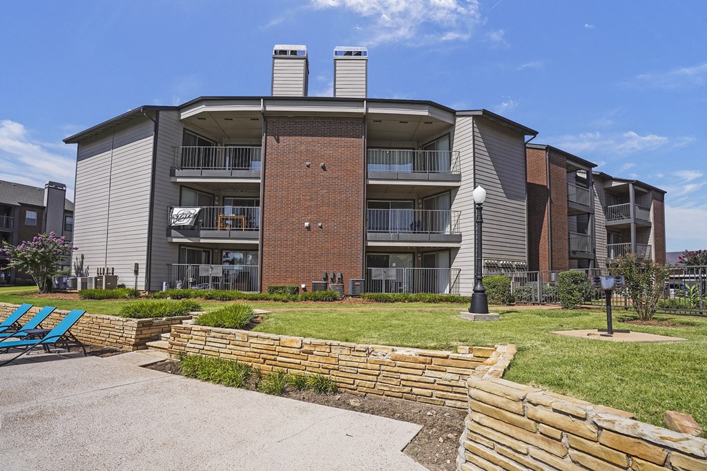 A modern apartment building with a brick chimney and a small garden in front.