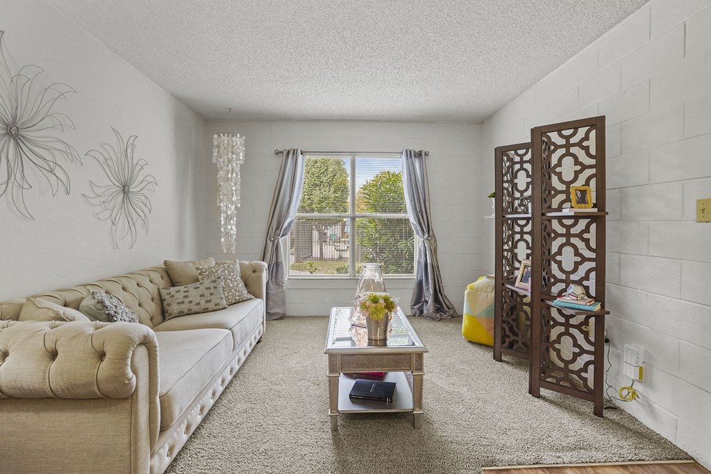 A living room with a beige sofa, a coffee table, and a large window with curtains.